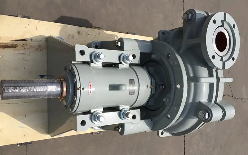 Gray horizontal slurry pump with extended shaft and flanged connections, on wooden pallet.