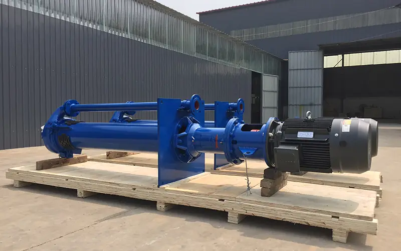 Two blue vertical slurry pumps with motor drives, mounted on wooden pallets in factory.