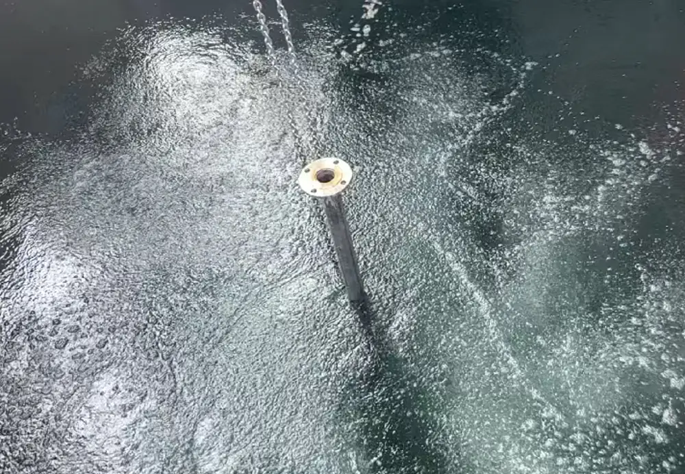 a top down view of turbulent wastewater actively aerated and churning around a suspended stainless steel diffuser lance with a perforated top plate.