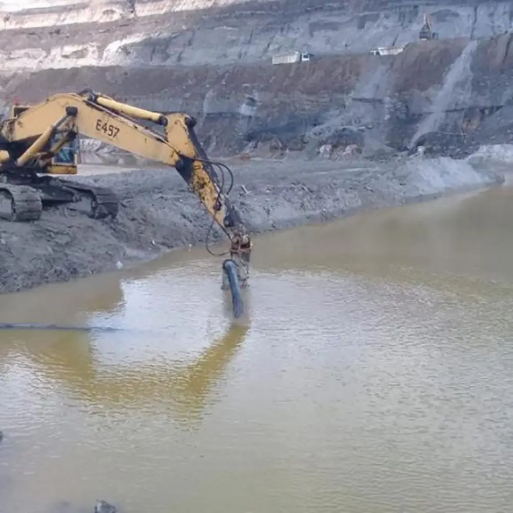 Excavator-mounted submersible sewage pump draining water from an open-pit mining site