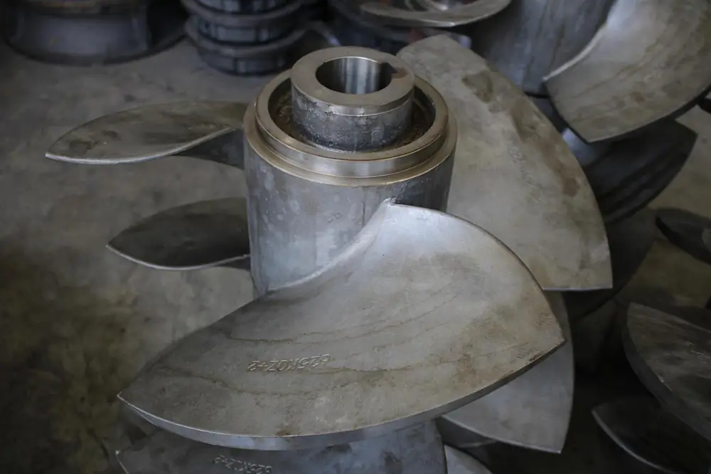 Large metal propeller-style impeller with curved blades and a central shaft hub in an industrial manufacturing facility.