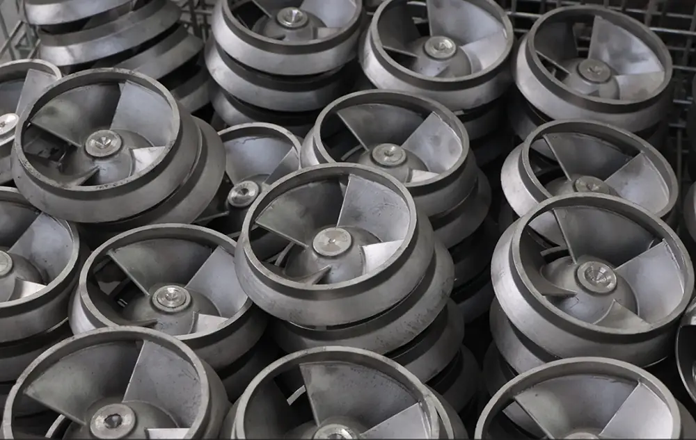 Multiple metal centrifugal pump impellers with curved blades stacked together in an industrial manufacturing facility.